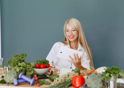 Woman using a tablet surrounded by fresh vegetables at a table, showcasing healthy lifestyle and technology.